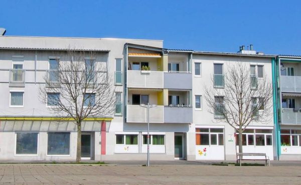 Mehrstöckiges Wohngebäude mit Balkonen und kahlen Bäumen vor einem klaren blauen Himmel.