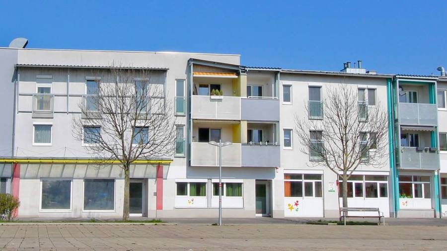 Mehrstöckiges Wohngebäude mit Balkonen und kahlen Bäumen vor einem klaren blauen Himmel.