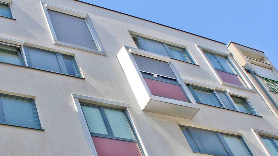 Moderne Wohnhausfassade mit mehreren Fenstern und Balkonen unter blauem Himmel.
