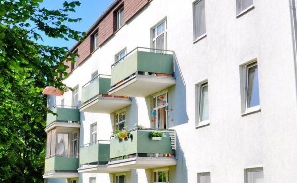 Wohngebäude mit grünen Balkonen und Baum in sonniger Lage, ideal für Wohnungskauf in Wien.