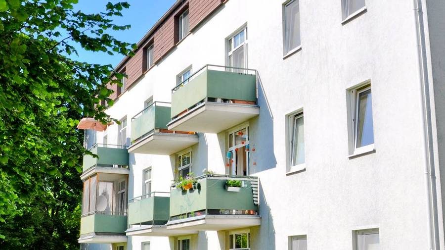 Wohngebäude mit grünen Balkonen und Baum in sonniger Lage, ideal für Wohnungskauf in Wien.