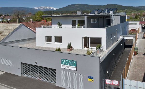 Moderne Wohnanlage vor Berglandschaft mit blauen Himmel und Schnee in der Ferne. Gebäude mit Solarpanels.