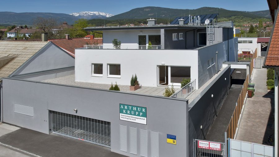 Moderne Wohnanlage vor Berglandschaft mit blauen Himmel und Schnee in der Ferne. Gebäude mit Solarpanels.