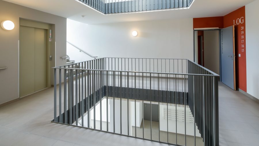 Modernes Treppenhaus mit Aufzug und Geländer in einem Gebäude, minimalistisches Design, hell erleuchtet.