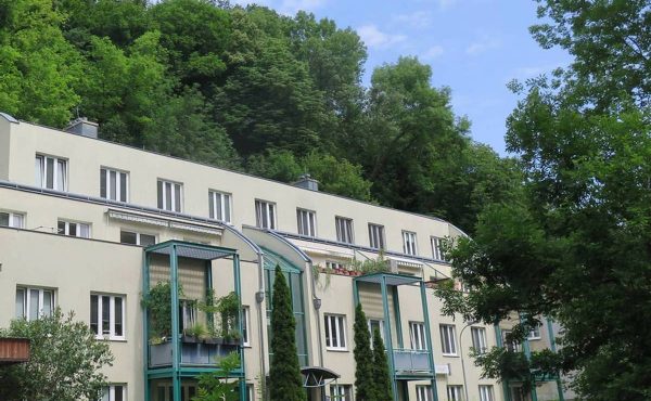 Wohngebäude umgeben von Bäumen mit Balkonen und Natur im Hintergrund.