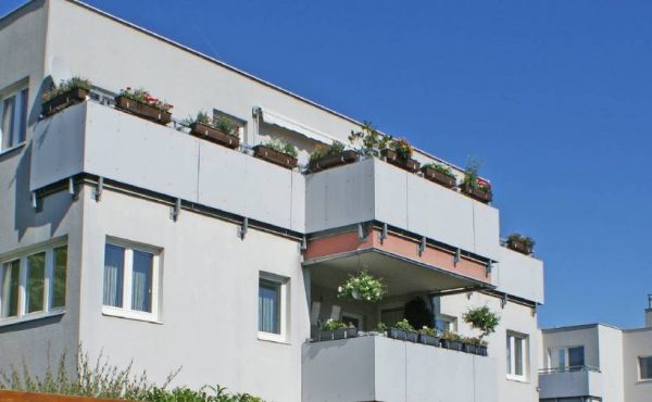 Moderne Wohngebäude mit Balkonen und Pflanzen unter blauem Himmel.