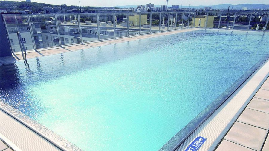 Dachterrassen-Pool mit Stadtblick und Glasgeländer bei klarem Himmel.