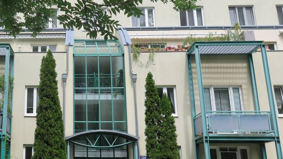 Moderne Stadthausfassade mit großen Glasfenstern und Balkonen, idyllische Lage in Wien.