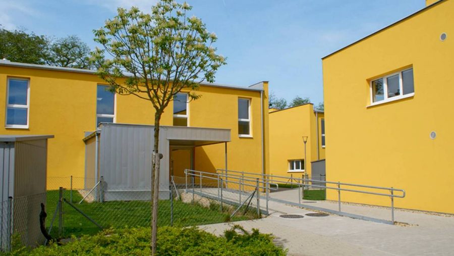 Moderne gelbe Reihenhäuser mit Garten und Gehweg, ideale Wohngegend in Wien.