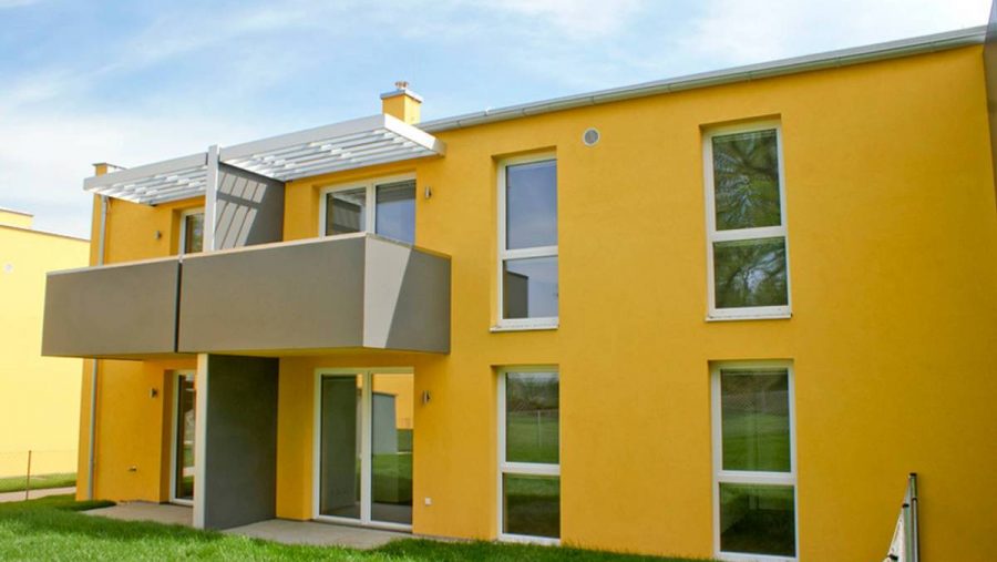 Modernes gelbes Haus mit Balkon und Garten, ideal für Wohnung kaufen in ruhiger Lage.