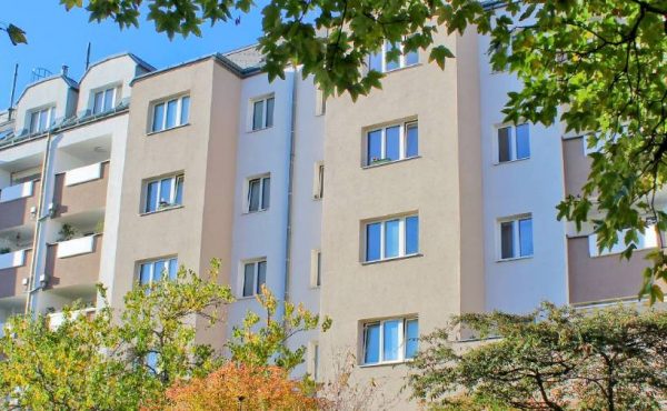 Moderne Wohngebäude mit mehreren Stockwerken, umgeben von Bäumen, an einem sonnigen Tag.