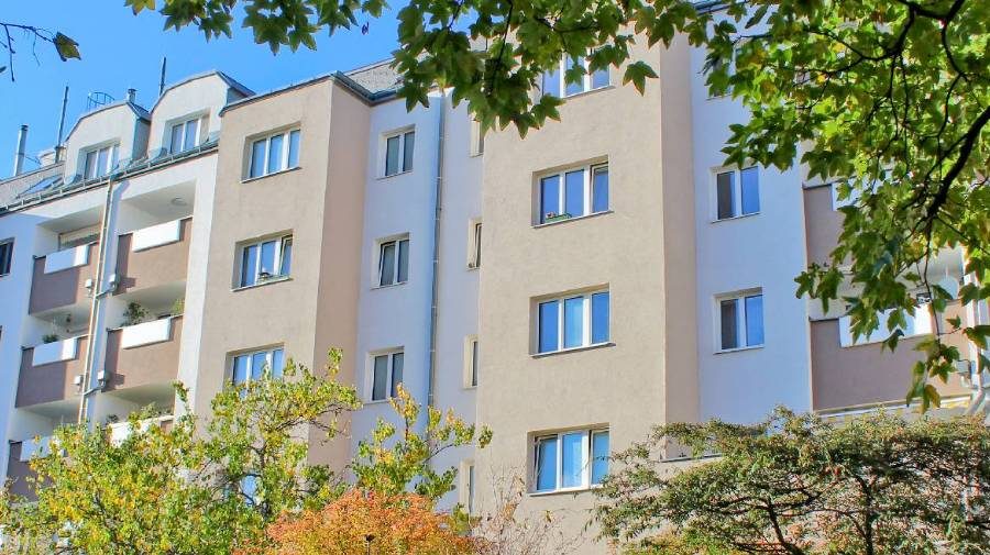 Moderne Wohngebäude mit mehreren Stockwerken, umgeben von Bäumen, an einem sonnigen Tag.