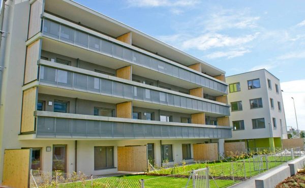 Mehrstöckiges Gebäude mit Balkonen, moderne Architektur, blauer Himmel im Hintergrund.