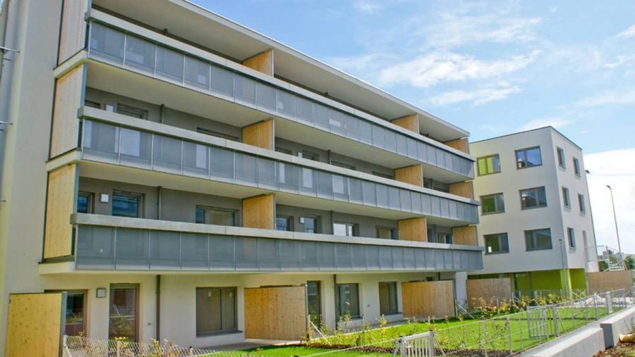 Mehrstöckiges Gebäude mit Balkonen, moderne Architektur, blauer Himmel im Hintergrund.
