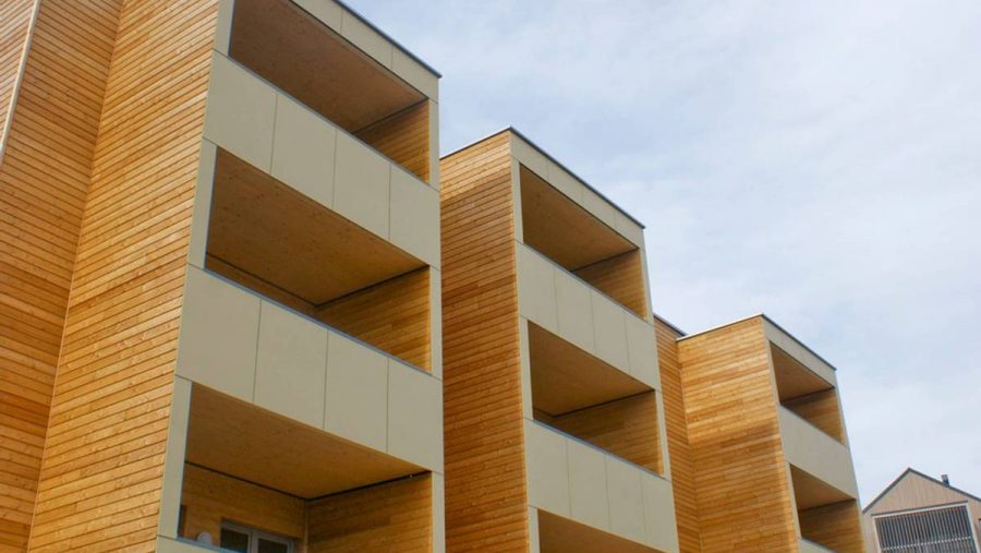 Mehrfamilienhaus mit Holzfassade und Balkonen in moderner Architektur. Ideal für Wohnungskäufer in urbaner Lage.