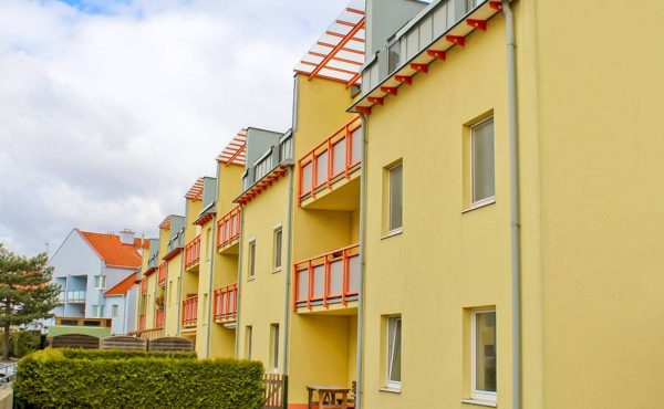 Mehrfamilienhaus mit Balkonen in gelber Fassade, ideal für Wohnungskauf in ruhiger Lage.