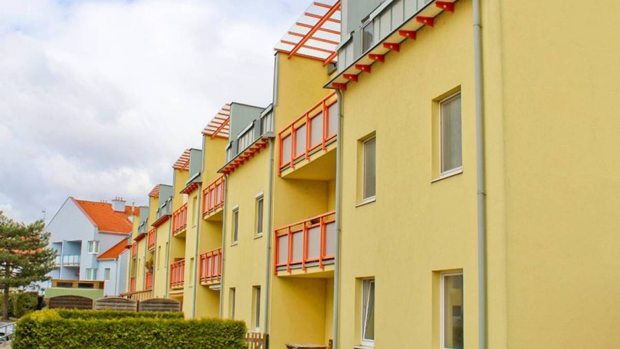 Mehrfamilienhaus mit Balkonen in gelber Fassade, ideal für Wohnungskauf in ruhiger Lage.