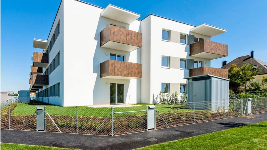 Modernes Mehrfamilienhaus mit weißen Wänden und Balkonen an einem sonnigen Tag, umgeben von grünem Rasen.
