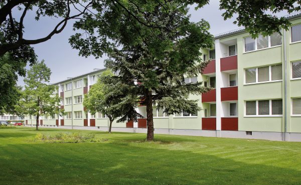 Mehrfamilienhaus mit grüner Fassade, umgeben von Bäumen und Rasenfläche.
