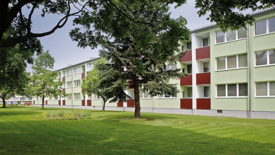Mehrfamilienhaus mit grüner Fassade, umgeben von Bäumen und Rasenfläche.