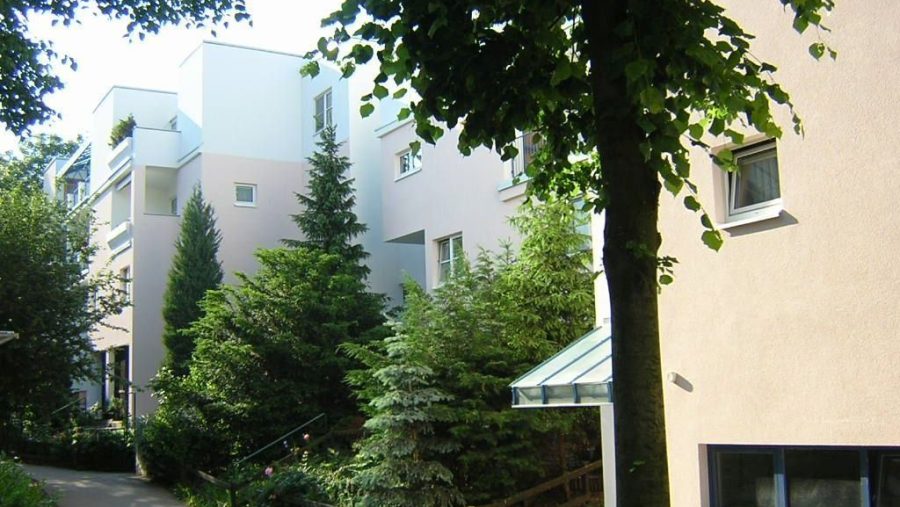 Moderne Wohngebäude mit Bäumen und Pflanzen im Vordergrund, sonniger Tag.