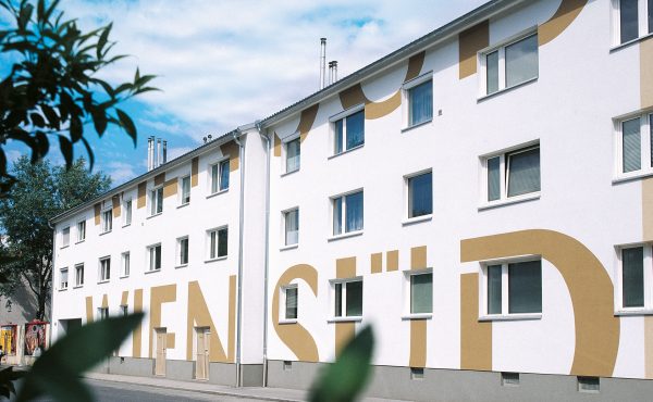Wohnhaus mit Schriftzug WIEN SÜD an der Fassade vor blauem Himmel und Bäumen.