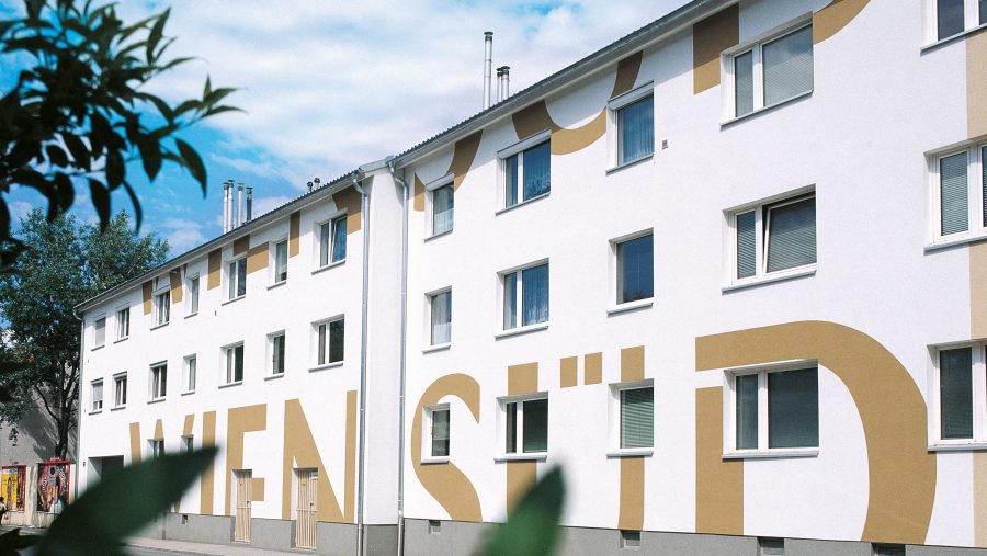 Wohnhaus mit Schriftzug WIEN SÜD an der Fassade vor blauem Himmel und Bäumen.