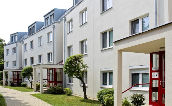 Mehrfamilienhaus mit moderner Architektur, helle Fassaden, gut gepflegte Grünanlagen, Wohngebäude in städtischer Umgebung.