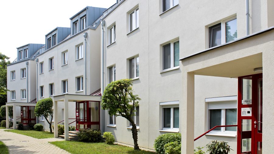 Mehrfamilienhaus mit moderner Architektur, helle Fassaden, gut gepflegte Grünanlagen, Wohngebäude in städtischer Umgebung.
