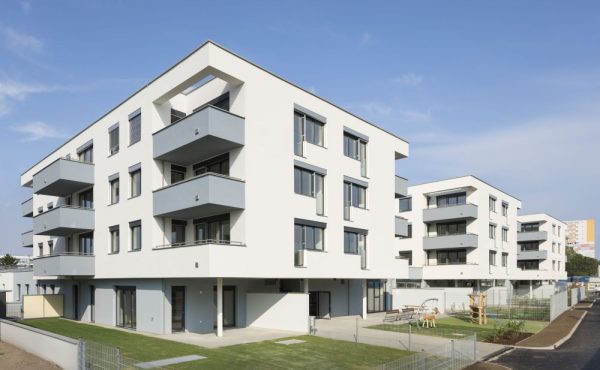 Moderne Wohngebäude mit Balkonen und grünem Außenbereich unter blauem Himmel.