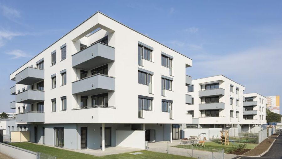 Moderne Wohngebäude mit Balkonen und grünem Außenbereich unter blauem Himmel.