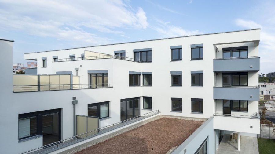 Modernes Wohngebäude mit weißer Fassade und Balkons unter blauem Himmel.