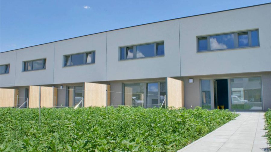 Mehrfamilienhaus mit moderner Fassade und grünem Vorgarten bei sonnigem Wetter.