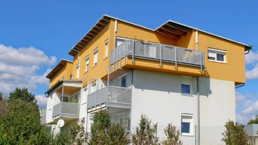 Moderne Wohngebäude mit gelber Fassade und Balkonen unter blauem Himmel.