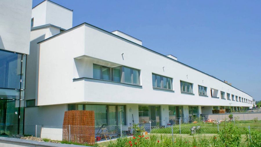 Moderne Wohnanlage mit weißen Fassaden und Gartenfläche, ideal für Immobilieninteressierte in Wien.