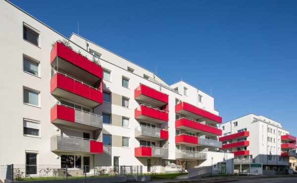 Moderne Wohngebäude mit roten Balkonen unter blauem Himmel.