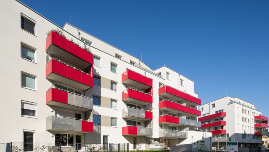 Moderne Wohngebäude mit roten Balkonen unter blauem Himmel.