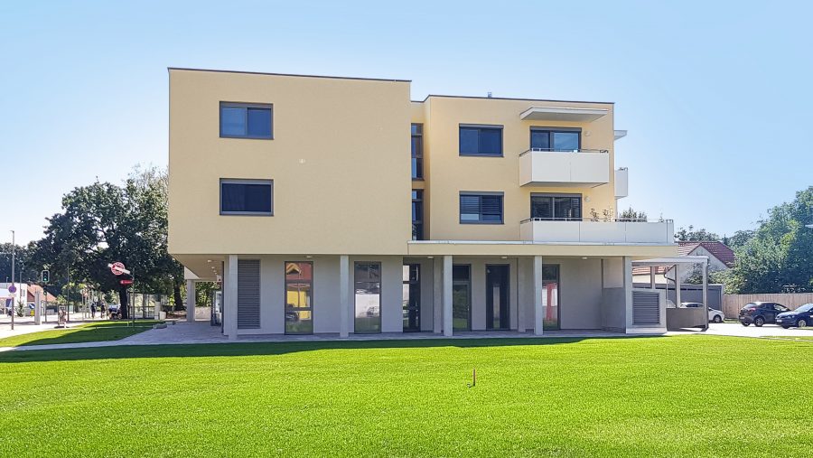 Moderne Wohngebäude mit Balkonen und grünem Rasen im Vordergrund bei Tageslicht.