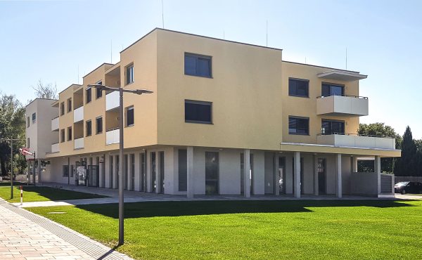 Modernes dreistöckiges Gebäudekomplex mit Balkonen und Rasenfläche bei Tageslicht.