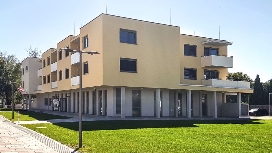 Modernes dreistöckiges Gebäudekomplex mit Balkonen und Rasenfläche bei Tageslicht.