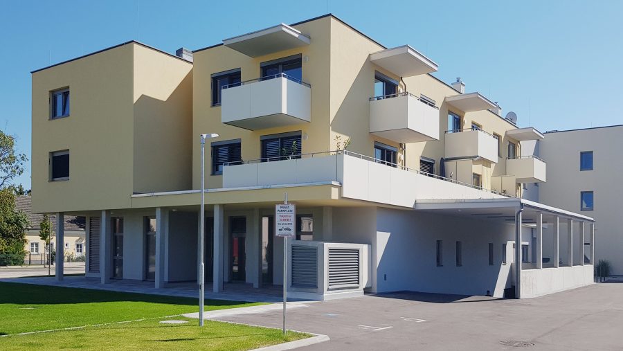 Moderne Wohngebäude mit Balkonen, sonniger Tag, blauer Himmel im Hintergrund.