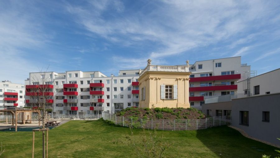 Moderne Wohnanlage mit historischem Pavillon, umgeben von Grünfläche und blauem Himmel im Hintergrund.