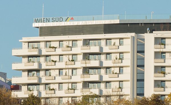 Moderne Wohnanlage mit Balkonen und grünen Elementen, blauer Himmel im Hintergrund.