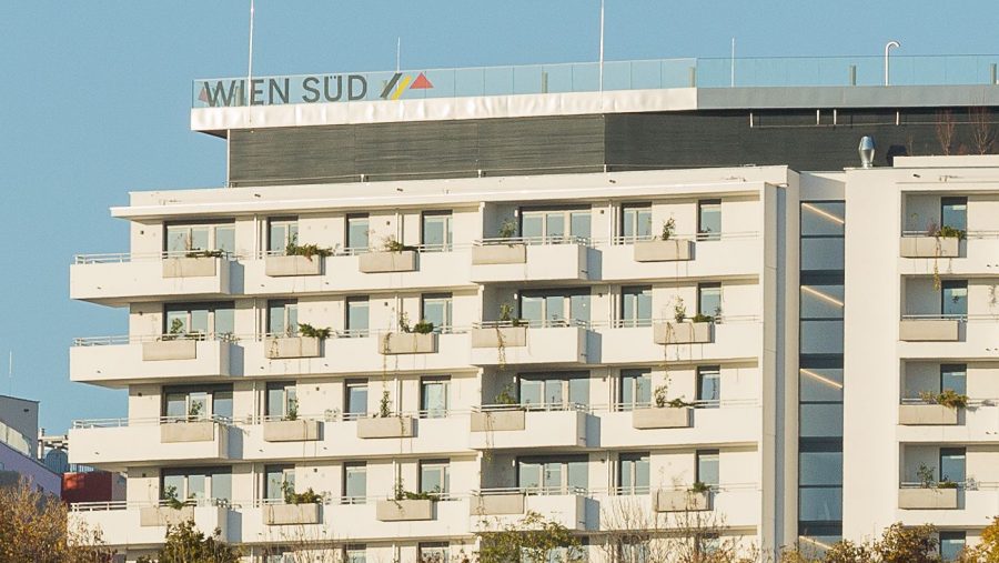 Moderne Wohnanlage mit Balkonen und grünen Elementen, blauer Himmel im Hintergrund.