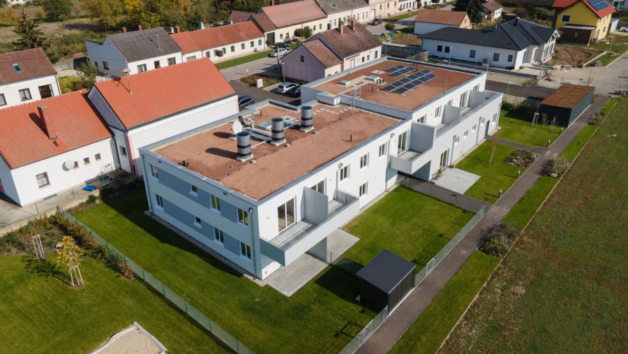 Moderne Wohngebäude mit begrünten Flächen und Solarpanels auf dem Dach in einer Nachbarschaft.