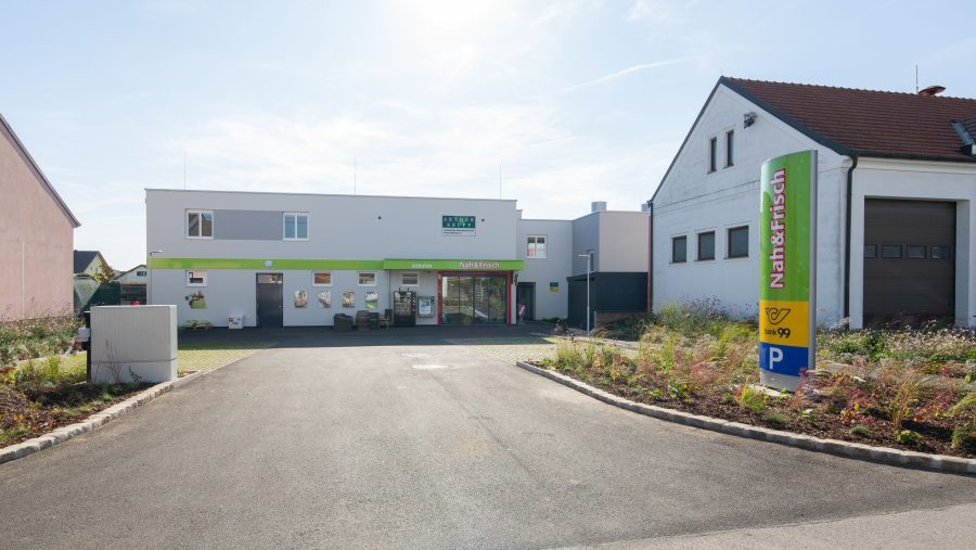 Geschäftsgebäude mit Parkplatz bei Tag, moderner Bau mit grünem Akzent, Nah&Frisch-Schild sichtbar.
