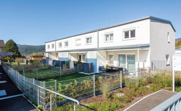 Moderne Reihenhäuser mit Garten und Bergblick bei sonnigem Wetter.