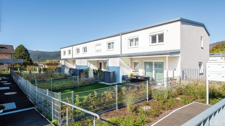Moderne Reihenhäuser mit Garten und Bergblick bei sonnigem Wetter.