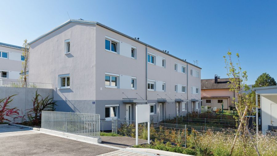 Wohnanlage mit modernen Reihenhäusern und Gärten an einem sonnigen Tag.