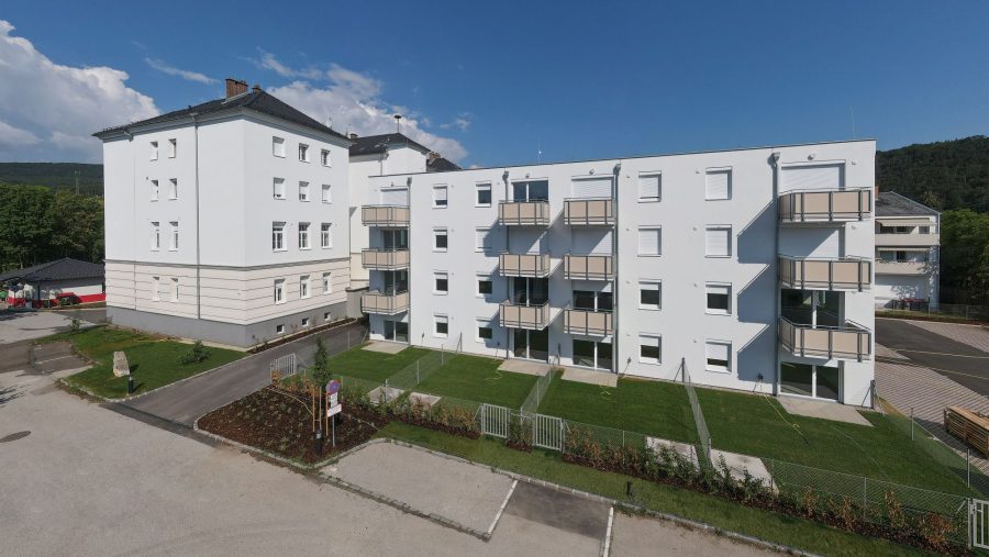 Mehrfamilienhäuser mit Balkonen und Grünflächen vor blauem Himmel.